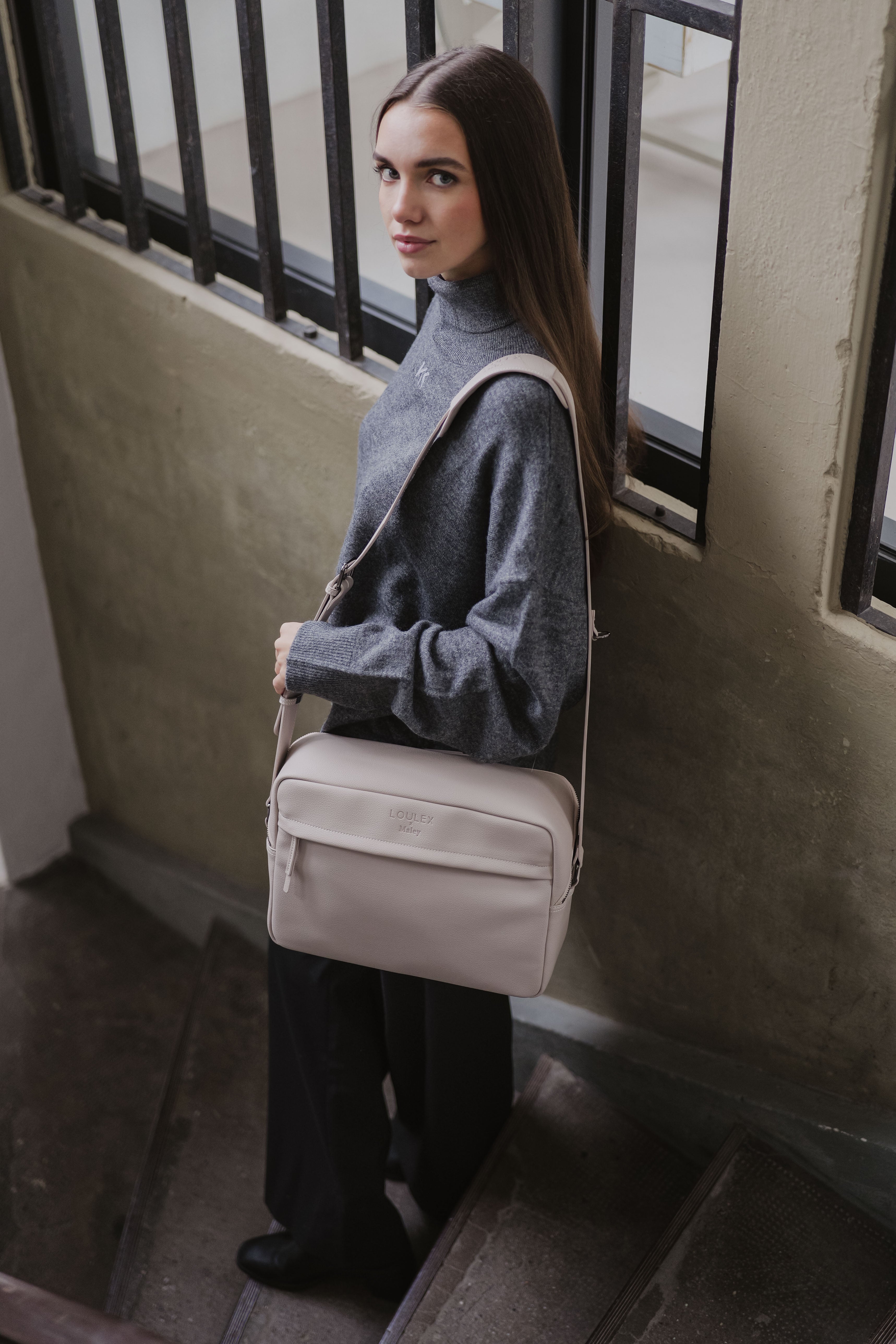 Woman holding a beige handbag in an indoor setting with a neutral color palette.