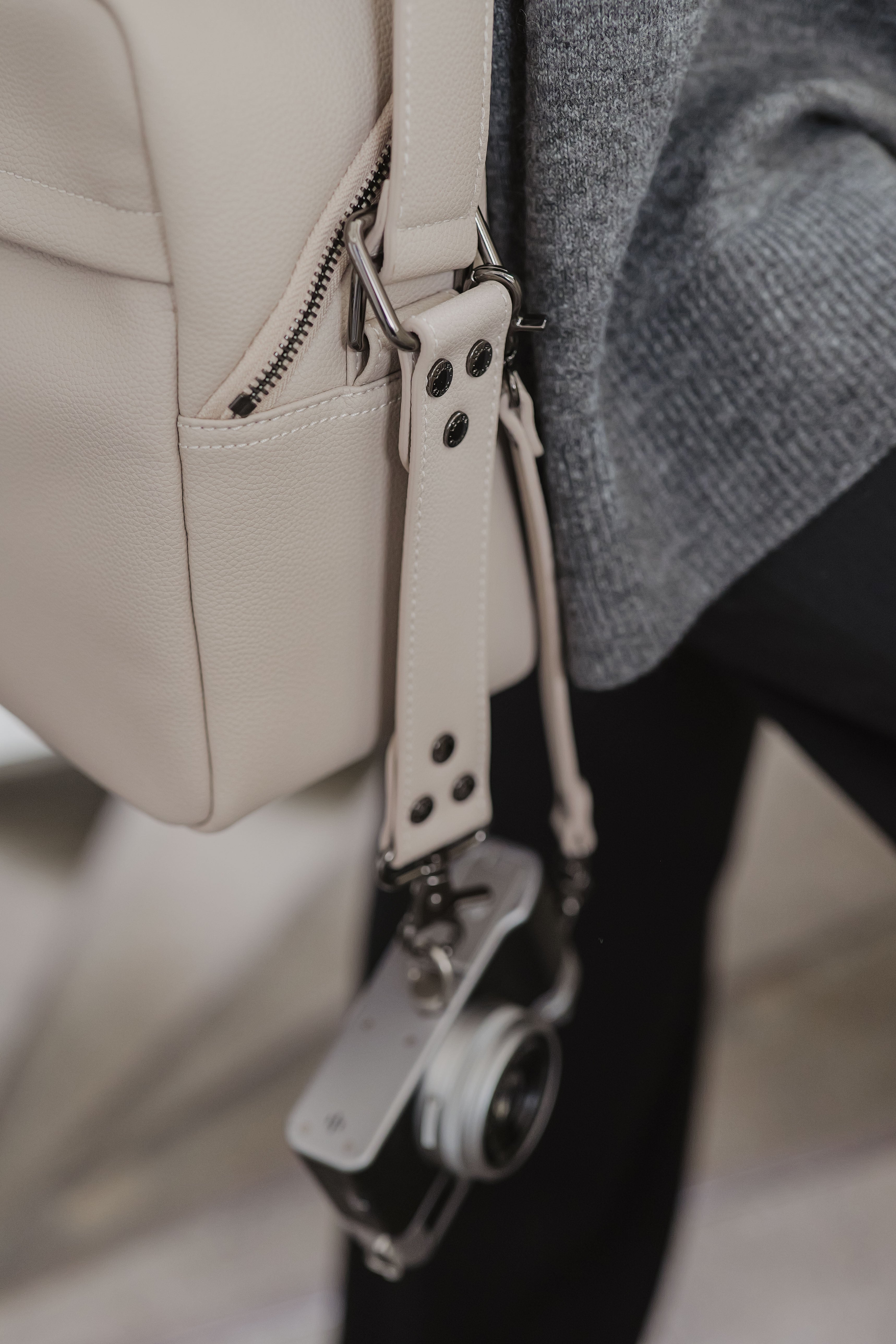 Close-up of a beige leather bag with a camera attached to its strap.