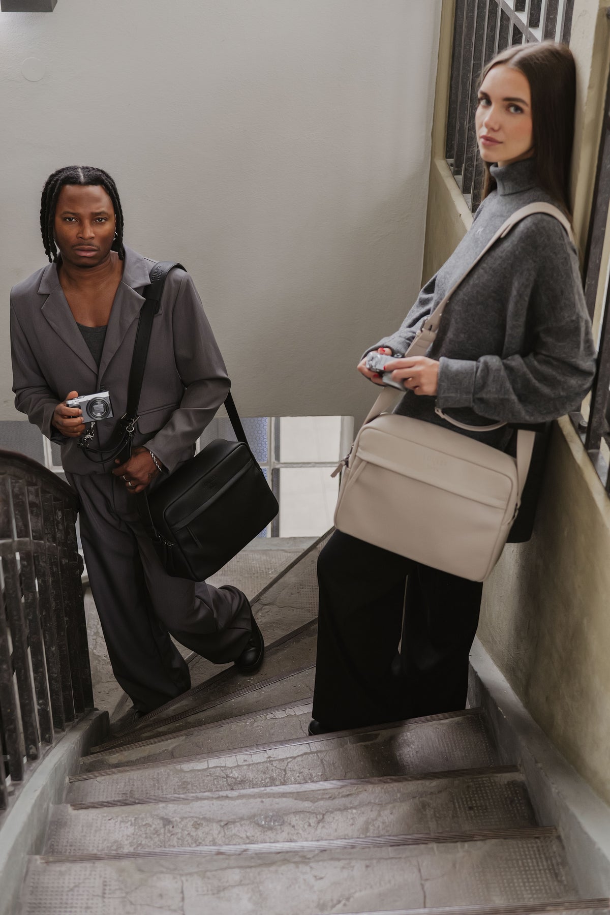 Two people standing on a staircase, one holding a camera and the other with a beige bag.