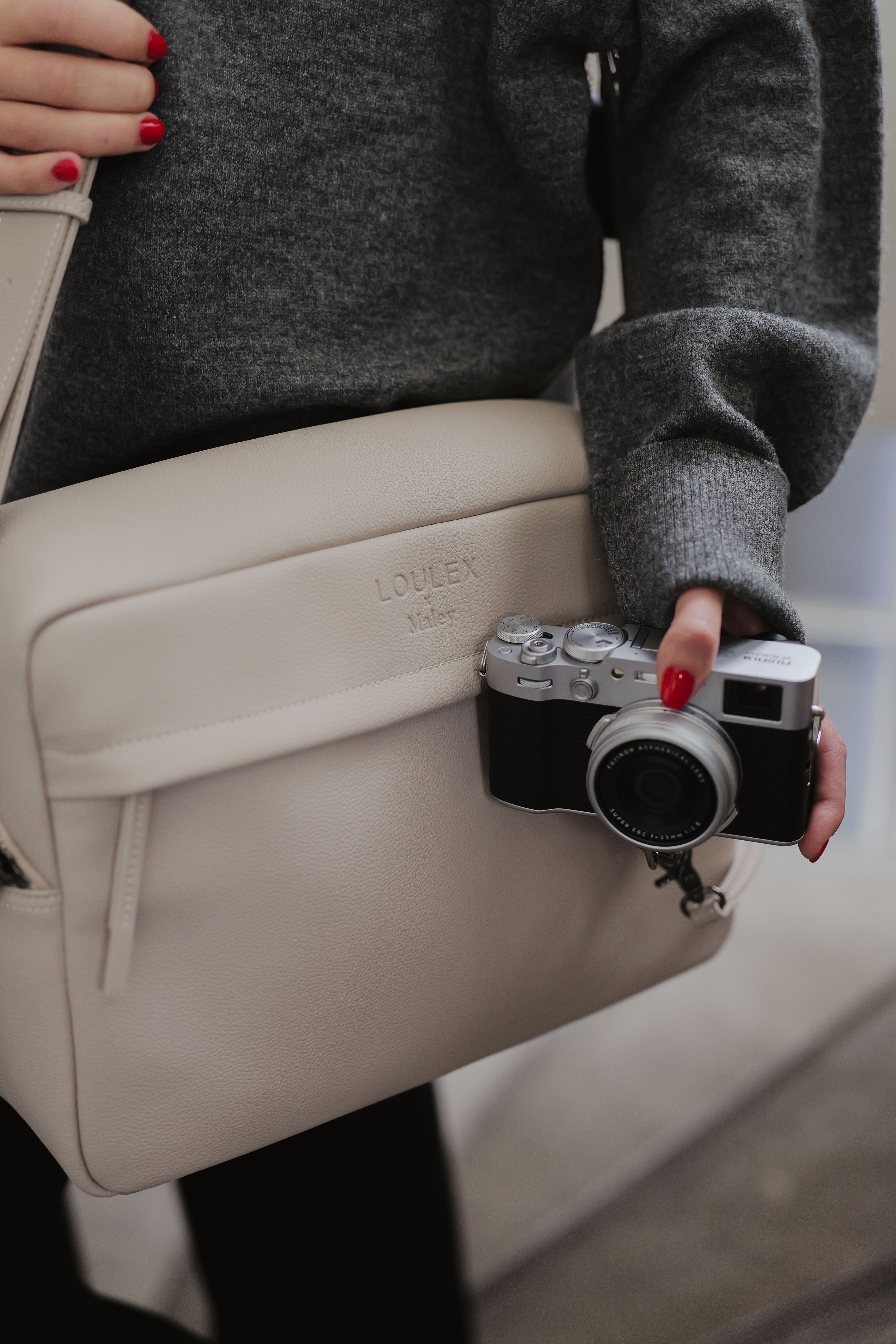 Person holding a beige bag with a camera attached, wearing a gray sweater.