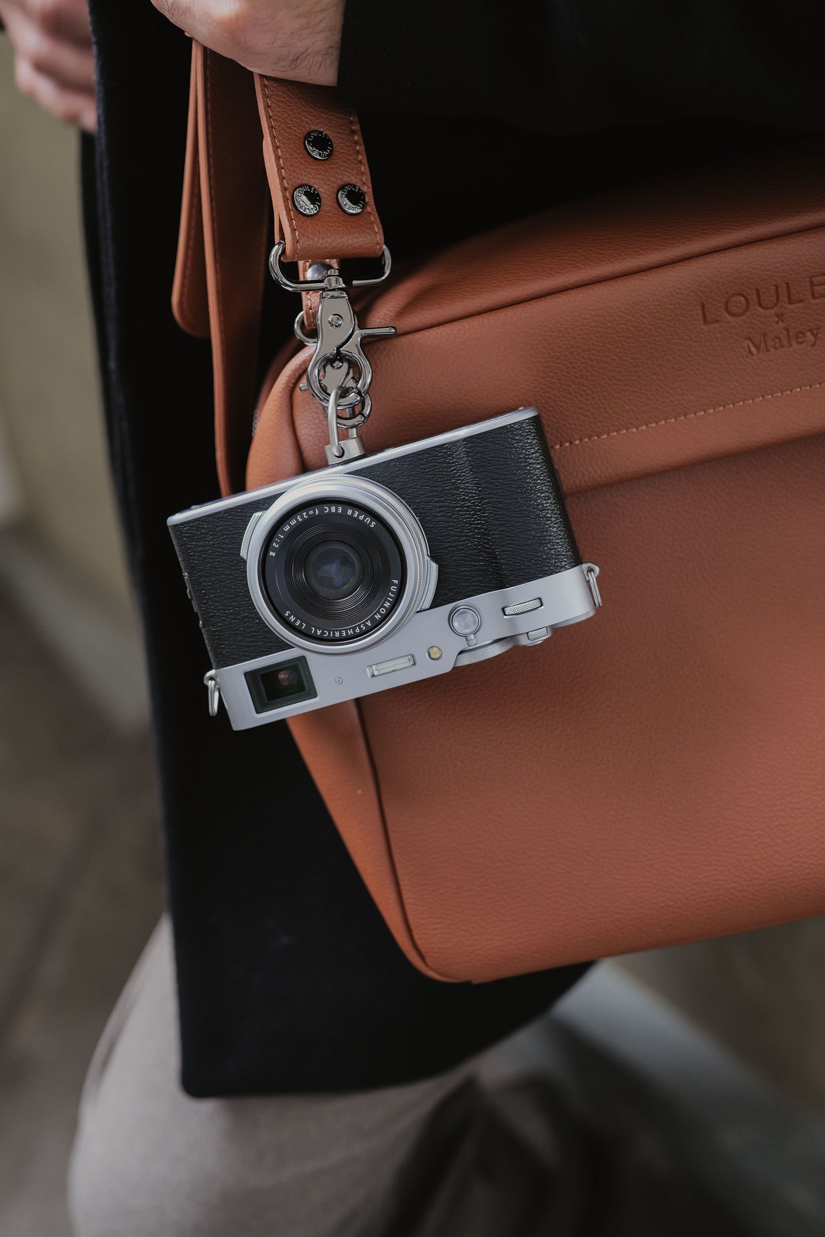 Camera-shaped keychain attached to a brown leather bag
