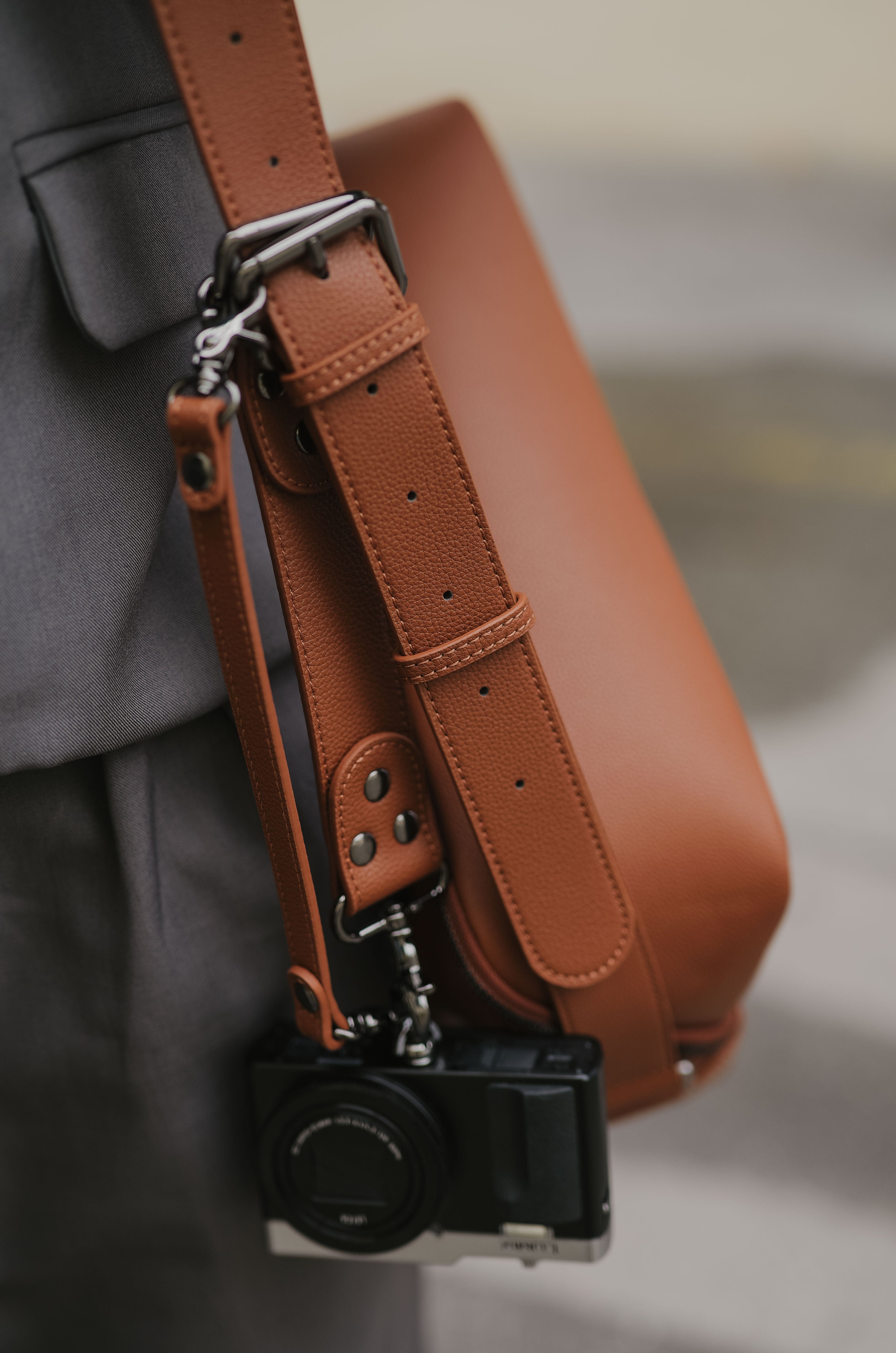 Brown leather bag with a camera attached to a strap, blurred background