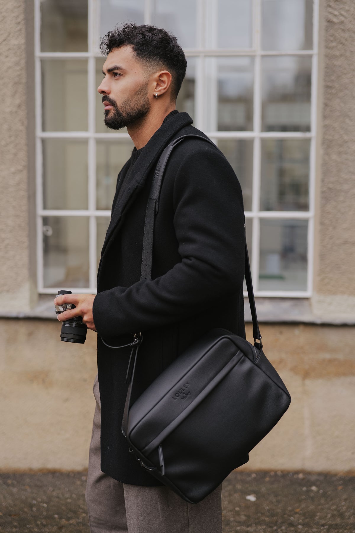 Man holding a black bag and a coffee cup outdoors.