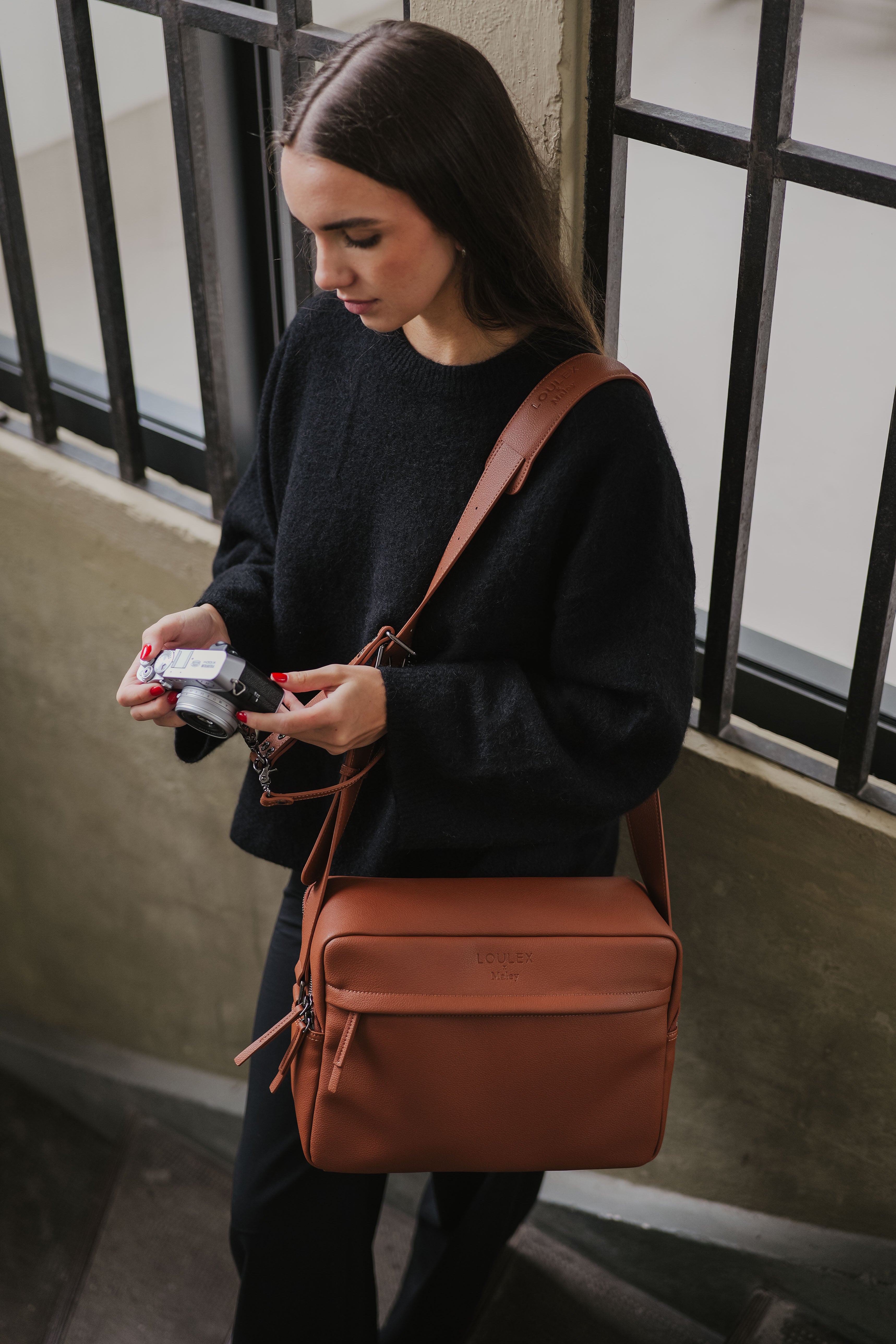 Woman holding a camera and a brown leather bag in an urban setting