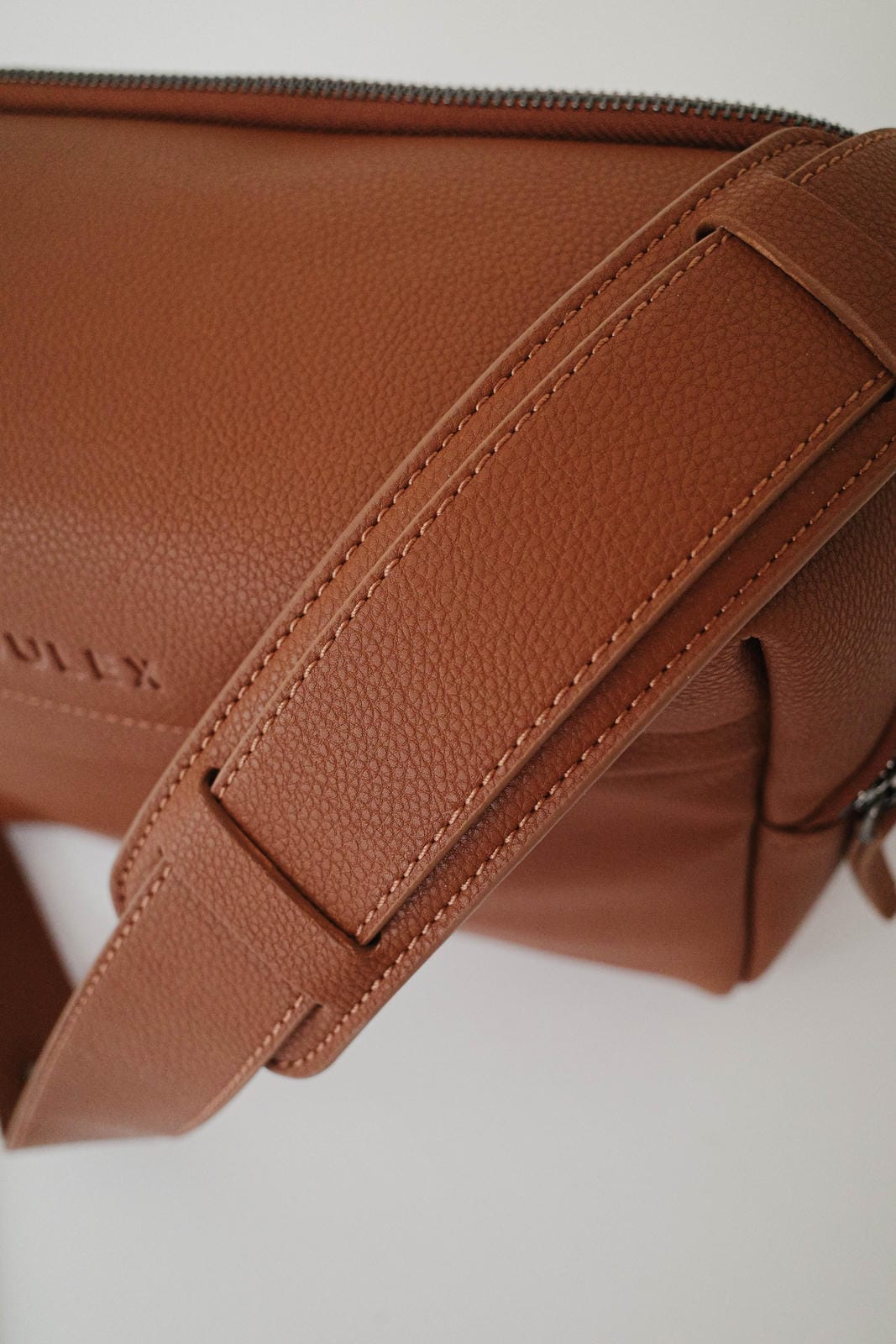 Close-up of a brown leather bag with visible branding on a light background