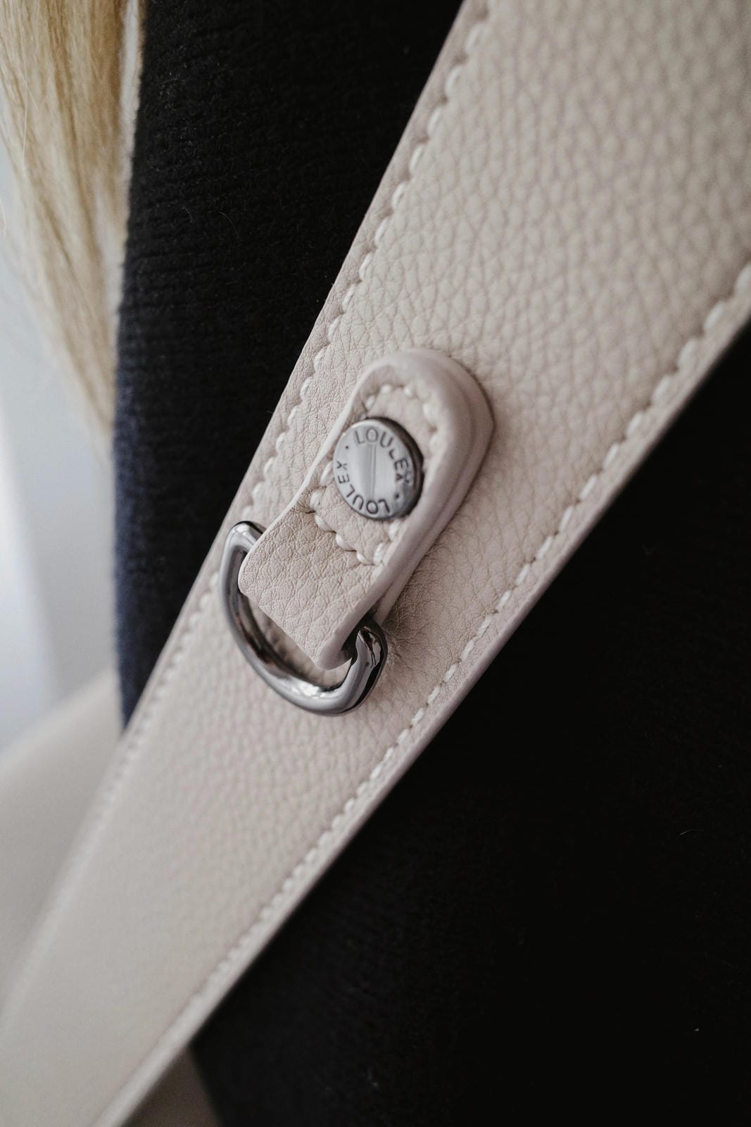 Close-up of a beige leather strap with a metal buckle on a black background