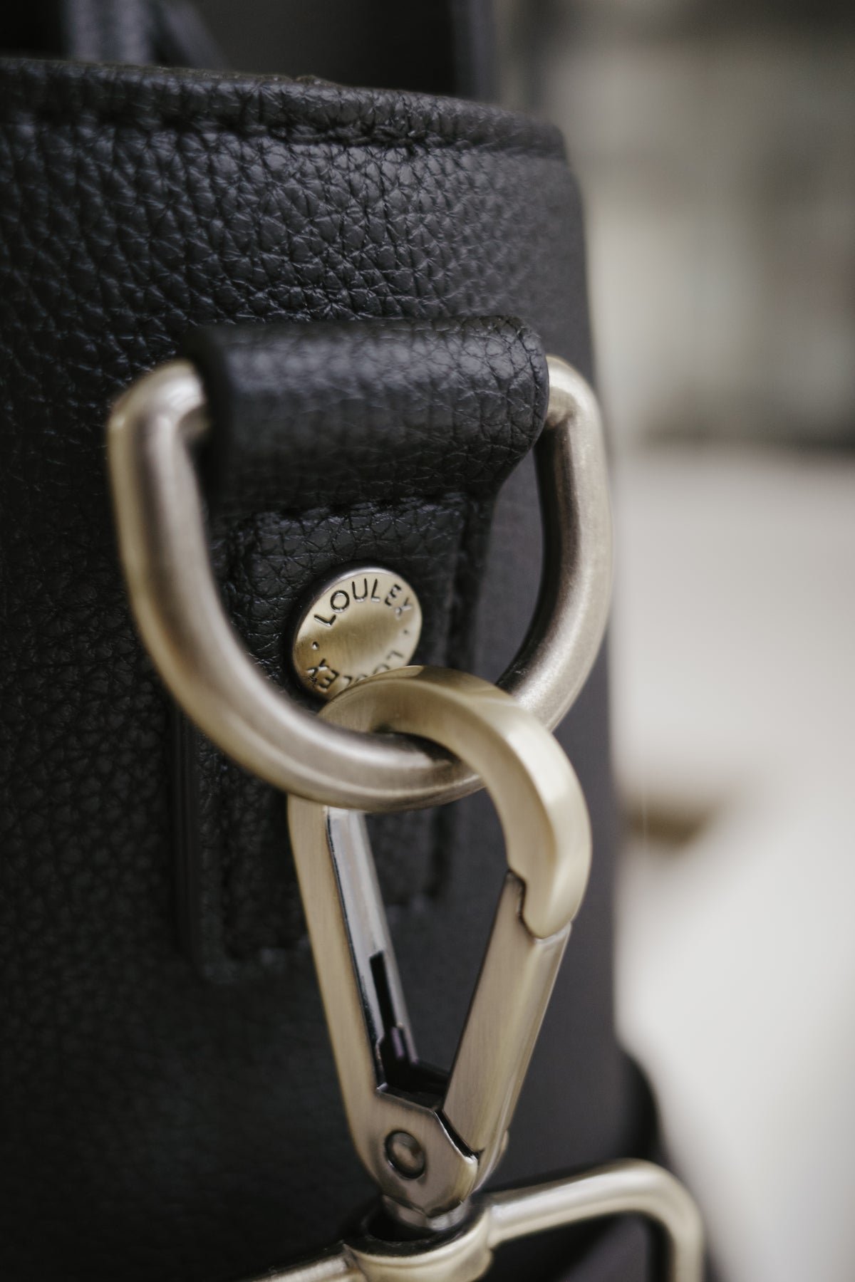 Close-up of a black leather bag with a gold carabiner and 'Louis Vuitton' logo.